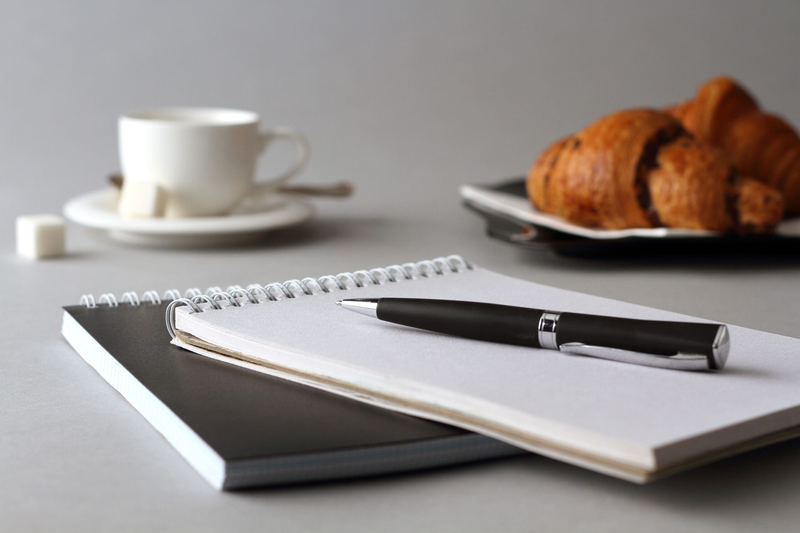 A notebook with a pen, a plate of croissants, and a mug of coffee
