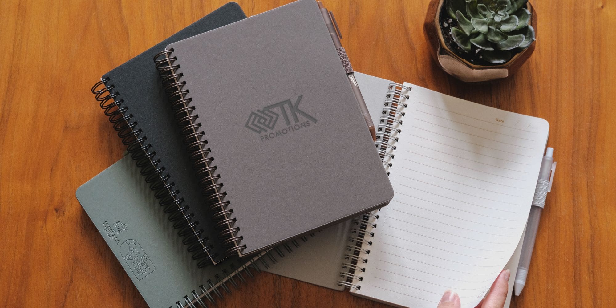 A desk with a collection of notebooks and a debossed TK Promotions logo