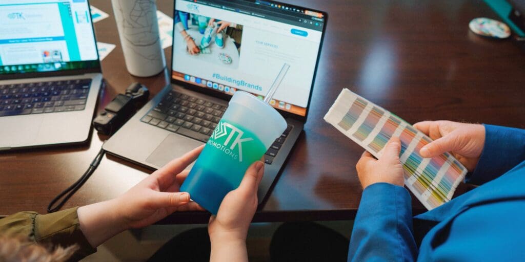 TK Promotions team comparing color swatches with a branded tumbler during the promotional product decoration process.